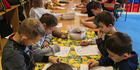 Powiększ grafikę: Grupa dzieci siedzi przy stole w świetlicy. Wszyscy w skupieniu rozwiązują wykreślanki wyrazowe.