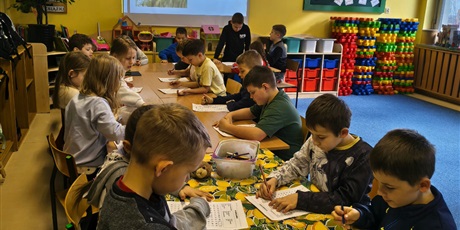 Powiększ grafikę: Grupa dzieci siedzi przy stole w świetlicy. Wszyscy w skupieniu rozwiązują wykreślanki wyrazowe.