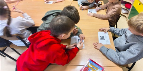 Powiększ grafikę: Dzieci siedzą przy stole i rozwiązują krzyżówki.