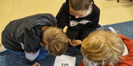 Powiększ grafikę: Trzech chłopców siedzi na dywanie.  Pochylają się nad kartką, na której znajduje się  krzyżówka.