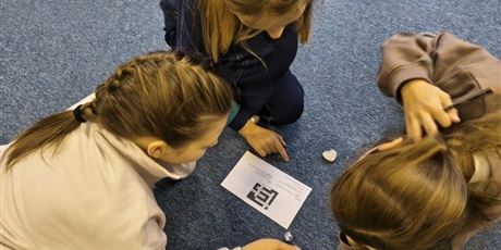 Powiększ grafikę: Trzy dziewczynki siedzą na dywanie.  Pochylają się nad kartką, na której znajduje się  krzyżówka.