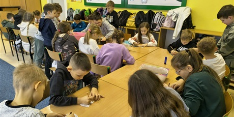 Powiększ grafikę: Grupa dzieci siedzi przy stole w świetlicy. W skupieniu kolorują obrazki.