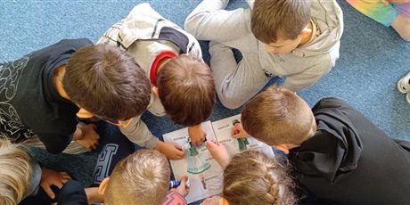 Powiększ grafikę:  Grupa dzieci w kole pochyla się nad plakatami ze strojami kaszubskimi. Przyklejają hasła z elementami strojów.