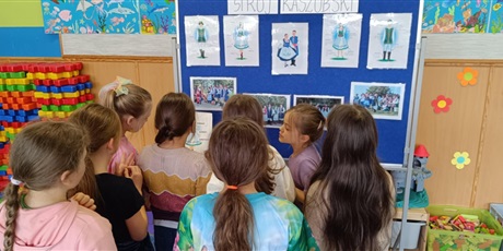 Powiększ grafikę: Grupa dziewczynek przygląda się tablicy informacyjnej ze zdjęciami strojów kaszubskich.