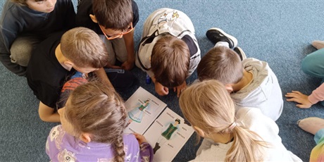 Powiększ grafikę: Grupa dzieci w kole pochyla się nad plakatami ze strojami kaszubskimi. Przyklejają hasła z elementami strojów.
