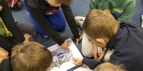 Powiększ grafikę: Grupa chłopców pochyla się nad plakatami, które leżą między nimi. Uczniowie przyklejają karteczki z nazwami poszczególnych elementów strojów kociewskich.