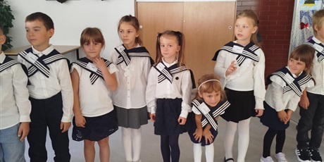 Powiększ grafikę: Dzieci oczekują na pasowanie. Ubrani są w stroje galowe i kołnierze marynarskie. Na twarzach widać skupienie i oczekiwanie.