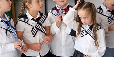Powiększ grafikę: Dzieci w strojach galowych z medalami założonymi na szyję oczekują na przejście do sali. Dzieci mają na sobie kołnierze marynarskie.