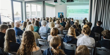 Powiększ grafikę: Sala wypełniona ludźmi siedzącymi na krzesłach, przed którymi na ścianie widać wyświetlaną prezentację.