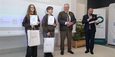 Powiększ grafikę: Uczniowie – zwycięzcy konkursu z dyplomami w rękach i dwaj panowie ogłaszający wyniki.