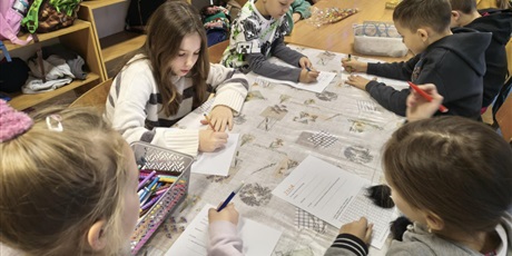 Powiększ grafikę: Grupa dzieci siedzi przy stole i rozwiązuje zadania dotyczące quizu wiedzy o kalendarzu.