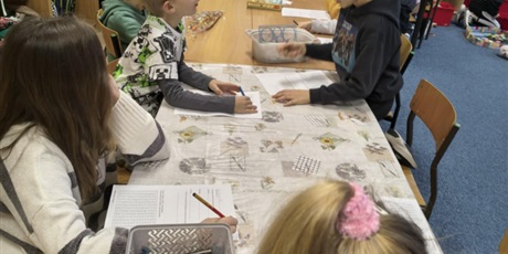 Powiększ grafikę: Grupa dzieci siedzi przy stole i rozwiązuje zadania dotyczące quizu wiedzy o kalendarzu.