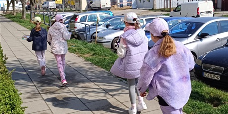 Powiększ grafikę: Cztery dziewczynki widoczne tyłem idą chodnikiem. Obok znajdują się samochody