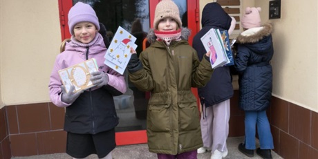 Powiększ grafikę: Dwie dziewczynki pozują do zdjęcia trzymając w rękach kartki bożonarodzeniowe. Pozostałe  dwie odwrócone są tyłem do obiektywu i wrzucają do skrzynek pocztowych kartki z życzeniami bożonarodzeniowymi.
