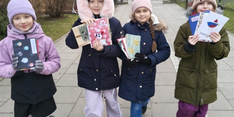 Powiększ grafikę: Cztery dziewczynki idą niosą  uniesione do góry kartki bożonarodzeniowe.