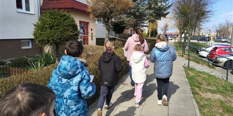 Powiększ grafikę: Grupa dzieci widoczna tyłem idzie chodnikiem. Obok znajdują się samochody.