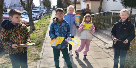 Powiększ grafikę: Dwie dziewczynki i trzech chłopców stoją na chodniku. W rękach trzymają kartki wielkanocne.