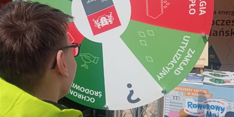 Powiększ grafikę: Chłopiec w okularach kręci kołem w loterii ekologicznej. W tle widać znak zapytania.