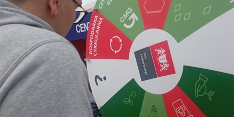 Powiększ grafikę: Chłopiec w szarej bluzie kręci kołem w loterii ekologicznej. W tle widać herb Gdańska.