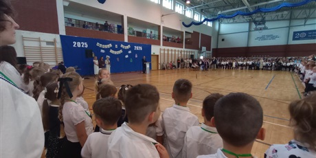 Powiększ grafikę: Sala gimnastyczna, na której są zebrani uczniowie. W tle widać przemawiającego dyrektora szkoły.