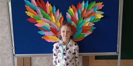 Powiększ grafikę: Dziewczynka w białej sukience pozuje do zdjęcia, w tle widać kolorowe skrzydła.