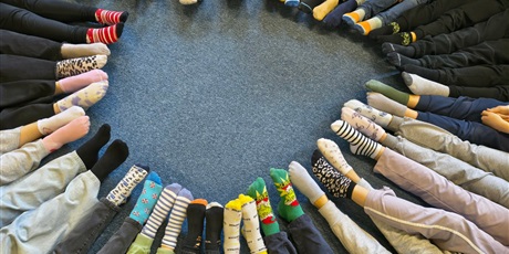 Powiększ grafikę: Na zdjęciu widoczne nogi z nałożonymi  kolorowymi skarpetkami na stopach. 