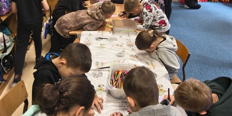 Powiększ grafikę: Duża grupa dzieci stoi lub siedzi przy stole w świetlicy. Dzieci piszą na kolorowych karteczkach życzliwe hasła i pozdrowienia.