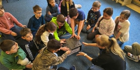 Powiększ grafikę: Grupa dzieci siedzi na dywanie i zamyka wieczko Kapsuły Czasu.