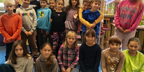 Powiększ grafikę: Grupa dzieci pozuje do zdjęcia. Za nimi znajduje się tablica informacyjna o przeciwdziałaniu przemocy rówieśniczej.