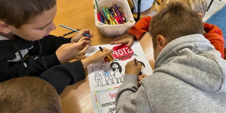 Powiększ grafikę: Czterech chłopców pochyla się nad przygotowywanym plakatem o przeciwdziałaniu przemocy rówieśniczej.