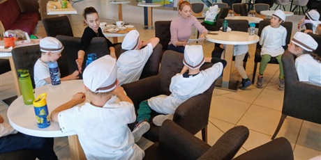 Powiększ grafikę: Nauczycielka czyta dzieciom legendę o gdańskim "Precelku, który uciekł z pieca". Nauczycielka i dzieci siedzą na brązowych krzesłach.