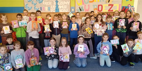 Powiększ grafikę: Dzieci w świetlicy pozują do zdjęcia grupowego. W rękach trzymają wykonane przez siebie kartki wielkanocne dla podopiecznych DPS OSTOJA w Gdańsku.
