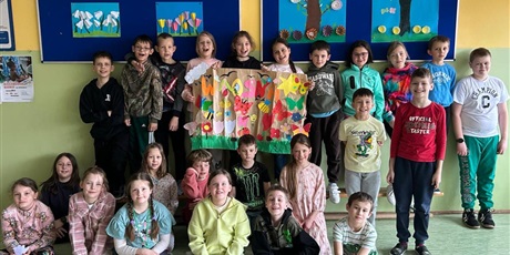 Powiększ grafikę: 10.	Dziewczynki i chłopcy oraz panie stoją i siedzą, pokazują nam serduszka utworzone rękami i trzymają plakat, który pokazuje sylwetkę Pani Wiosny w sukni z kwiatów.