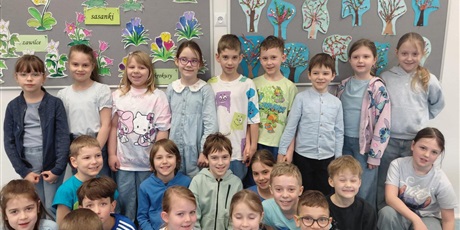 Powiększ grafikę: 12.	Dzieci stoją i trzymają dwa plakaty o wiośnie w parku i dwa rysunki, które pokazują drzewa i Panią Wiosnę.