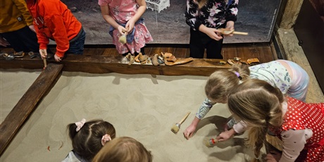 Powiększ grafikę: Grupa dzieci wykonuje zadania archeologa. Dzieci odkrywają ukryte rzeczy w piasku.