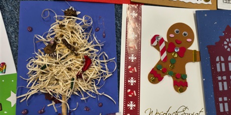 Powiększ grafikę: Dwie kolorowe kartki bożonarodzeniowe leżą na dywanie. Na jednej znajduje się wyklejona choinka a na drugiej ciastek z pianki.