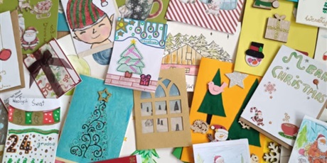 Powiększ grafikę: Kolorowe kartki bożonarodzeniowe leżą na dywanie. Są na nich namalowane i wyklejone bombki, choinki, bałwanki itp.