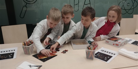 Powiększ grafikę: Dzieci układają puzzle. Chłopcy są pochłonięci pracą a dziewczynka się przygląda.