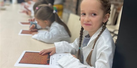 Powiększ grafikę: Dziewczynka ubrana w biały fartuch pozuje do zdjęcia. Uśmiecha się. Włosy ma uczesane w dwa warkoczyki.