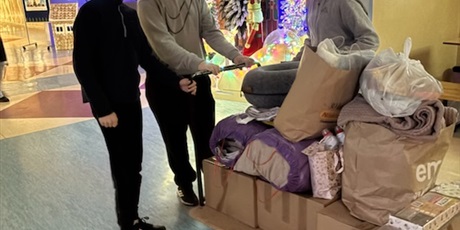 Powiększ grafikę: Trzej uczniowie przy wózku wypełnionym darami na korytarzu szkoły