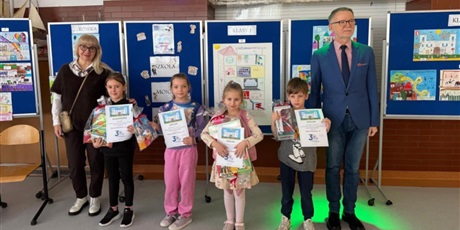 Powiększ grafikę: Laureaci konkursu "Szkoła moich marzeń" wraz z dyrekcją szkoły pozują do wspólnego zdjęcia. W rękach trzymają dyplomy i nagrody. Za nimi znajdują się granatowe tablice z pracami konkursowymi.