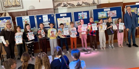 Powiększ grafikę: Laureaci konkursu "Szkoła moich marzeń" wraz z dyrekcją szkoły pozują do wspólnego zdjęcia. W rękach trzymają dyplomy i nagrody. Za nimi znajdują się granatowe tablice z pracami konkursowymi.