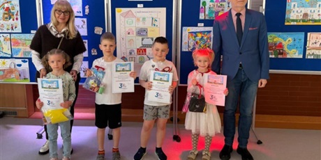 Powiększ grafikę: Laureaci konkursu "Szkoła moich marzeń" wraz z dyrekcją szkoły pozują do wspólnego zdjęcia. W rękach trzymają dyplomy i nagrody. Za nimi znajdują się granatowe tablice z pracami konkursowymi.